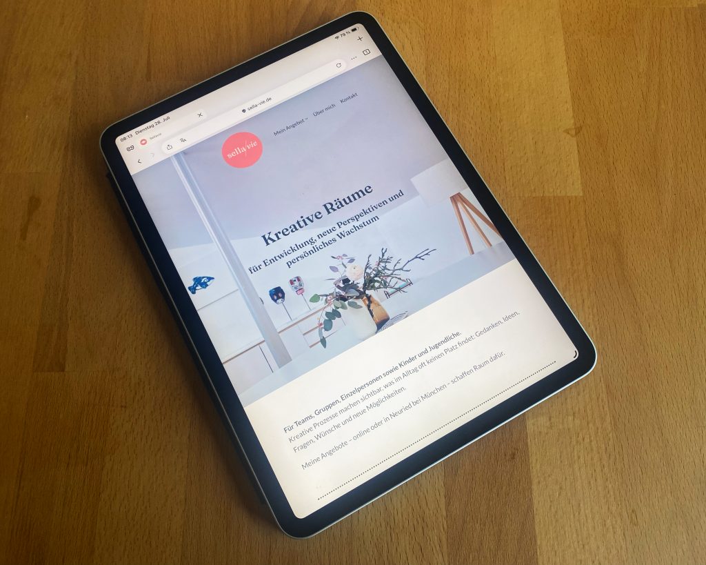 Holztisch, auf dem, schräg von unten fotografiert, ein ipad liegt. Darauf sieht man die neue Website von Gisela Knobbel, die klar und pastellig rüberkommt